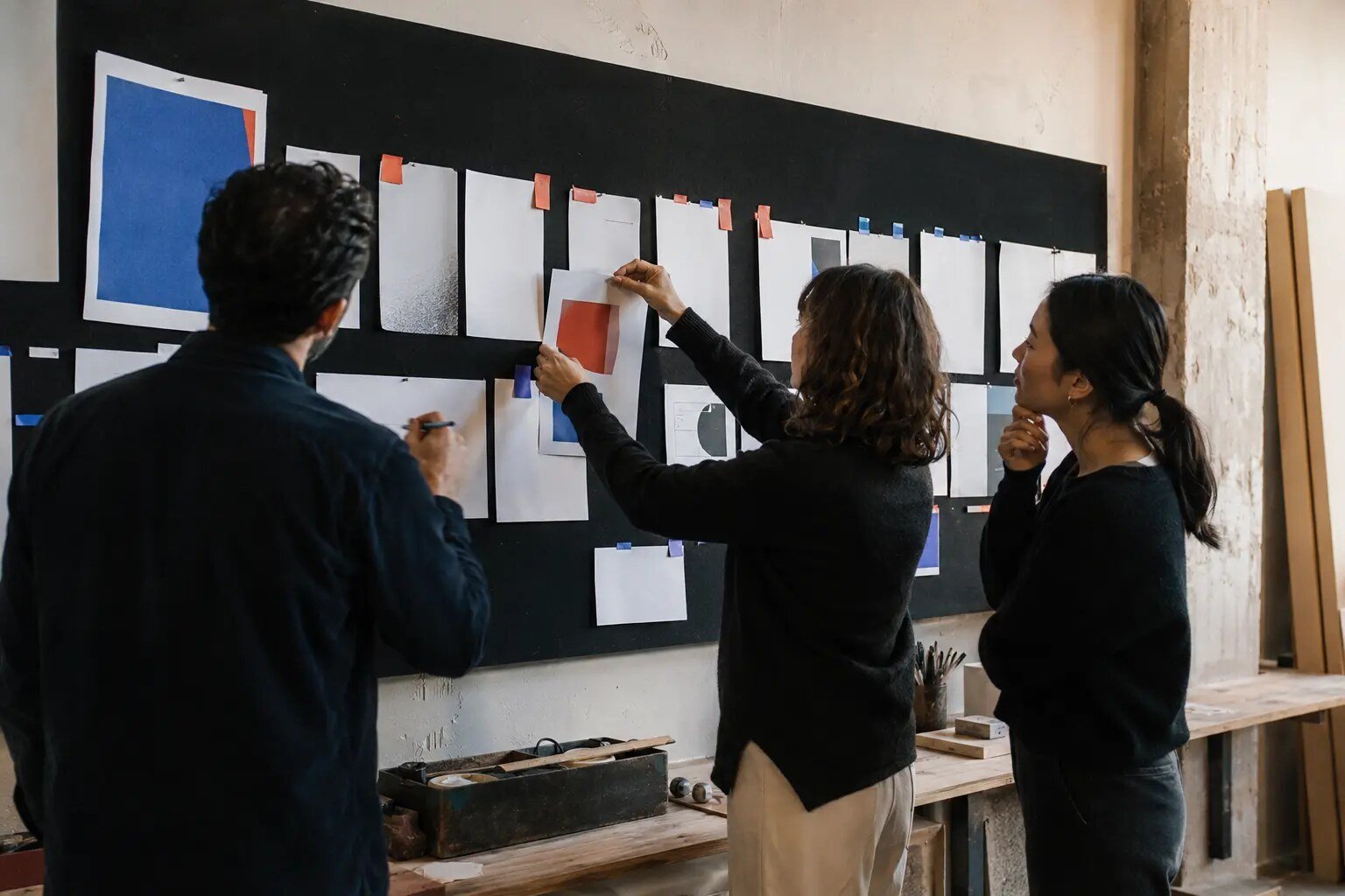 Three creative professionals sequencing campaign proofs on a studio pinboard
